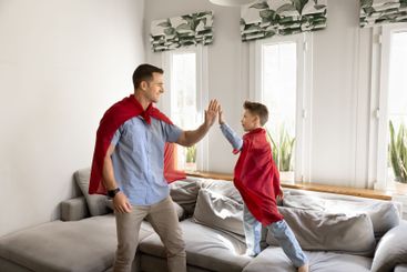 Positive dad and son in red superhero mantles playing game