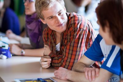 Handsome college student sitting in a classroom full of...