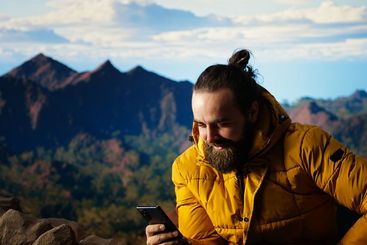 Traveler sitting and browsing his phone on the rocky...