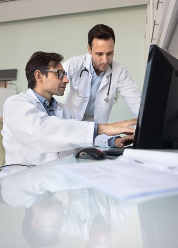 Team of two male doctors reviewing medical case at computer