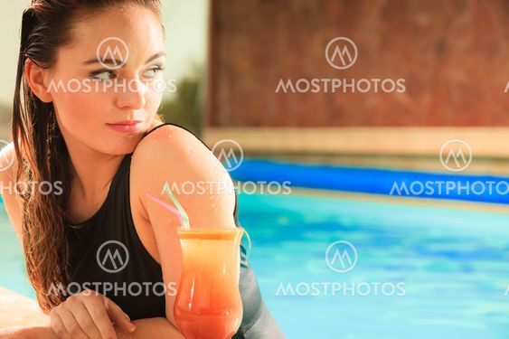 Woman with cocktail drink at swimming pool edge.