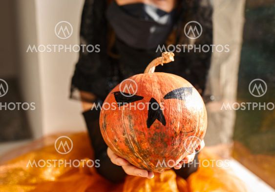 Girl in mask sitting at the window at home in halloween...