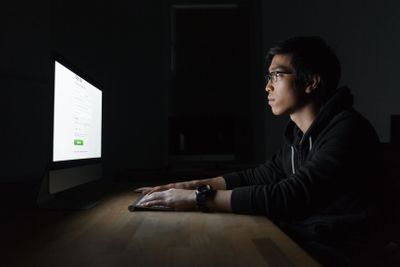 Handsome asian young man using computer in dark room