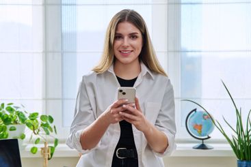 Confident young woman with smartphone in home interior