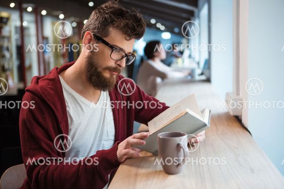 Clever boy in glasses reading book sitting at the desk