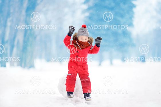 Little boy in red winter clothes having fun with snowball