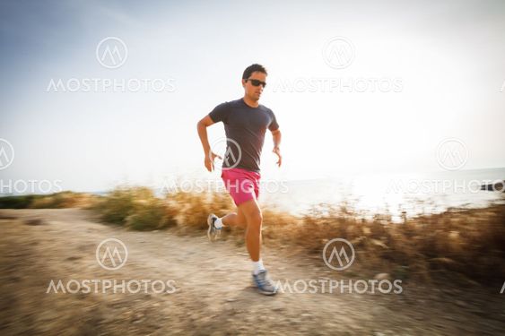 Caucasian young man running on a seacost path on a lovely summer evening, training for marathon (motion blurred image)