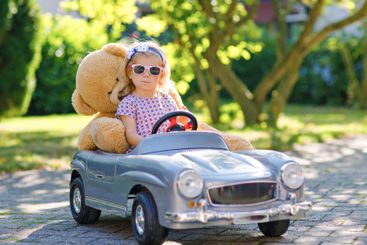 Little adorable toddler girl driving big vintage toy car...