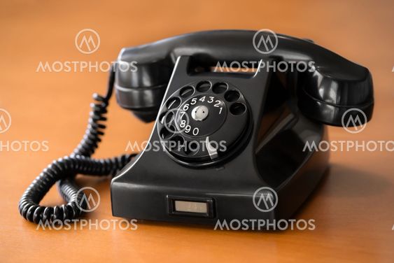 Old rotary dial phone on wooden desk
