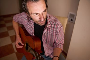 Man sitting playing acoustic guitar in a cozy indoor...