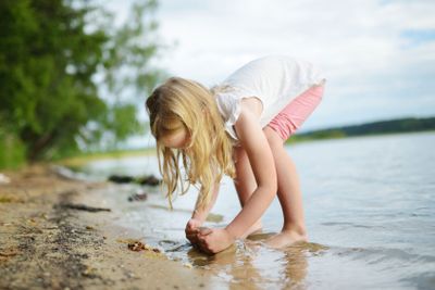 Cute young girl having fun on a sandy lake beach on warm...