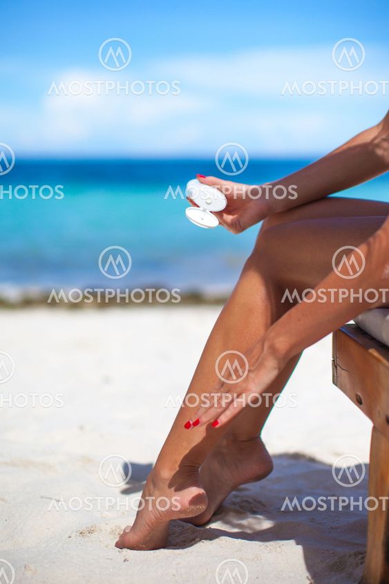 Young woman apply cream on her smooth tanned legs at tropical beac