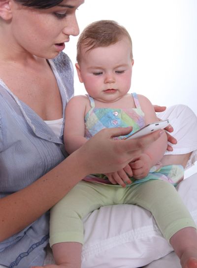 Mother resting baby on knee whilst looking at mobile...