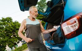 Grey senior sportsman getting badminton rackets out of...