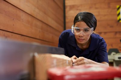 Female Carpenter Using Plane In Woodworking Woodshop