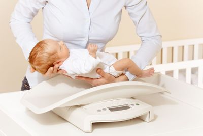 Mother put little newborn baby infant boy on scale