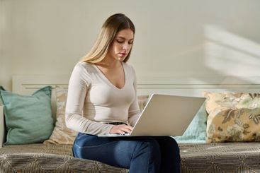 Young woman working at home, sitting on couch using laptop