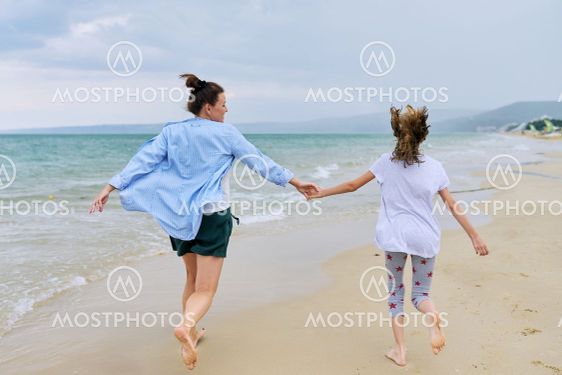 Happy mom and daughter running on the sea beach holding...