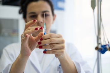 A focused nurse in a white lab coat carefully prepares a...