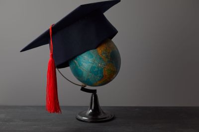 Academic cap with red tassel on globe on dark surface