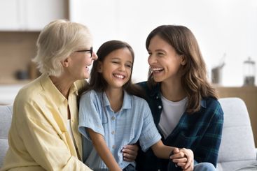 Joyful young mom and senior grandma cuddling kid girl