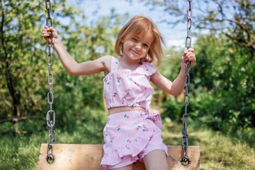 Little girl is rocking  on swing in summer garden