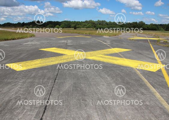 Yellow painted cross on asphalt with clouds in background