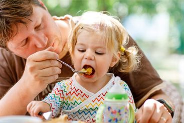 Young middle-aged father feeding cute little toddler...