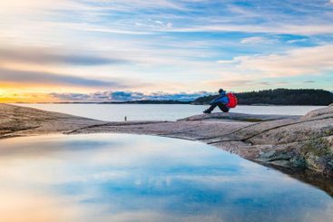 Man enjoys a tranquil sunset while seated on rocks by...