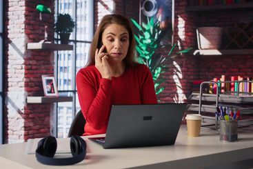 Focused woman in a home office loft talking on a mobile...