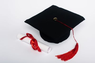 Black graduation cap with red tassel and diploma with...
