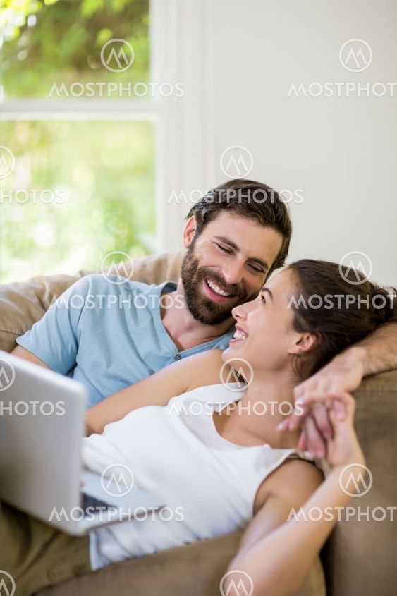 Happy couple lying on sofa and using laptop
