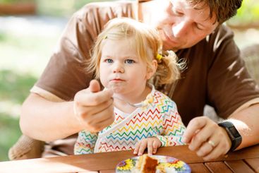 Young middle-aged father feeding cute little toddler...