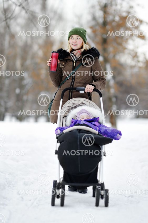 Young mother walking with baby in stroller in winter