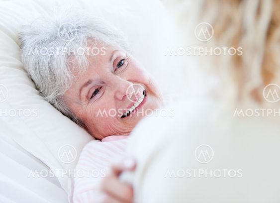 Cheerful senior woman lying on a hospital bed talking with her granddaughter