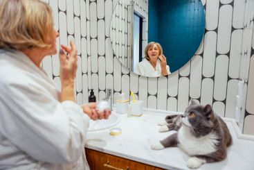 An elderly woman in a white housecoat applies cream on...