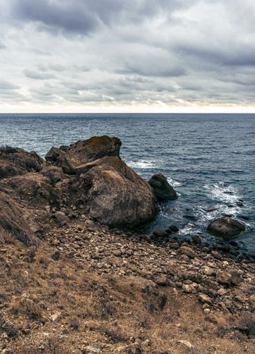 Cloudy skies over rocky coastline with waves crashing on...