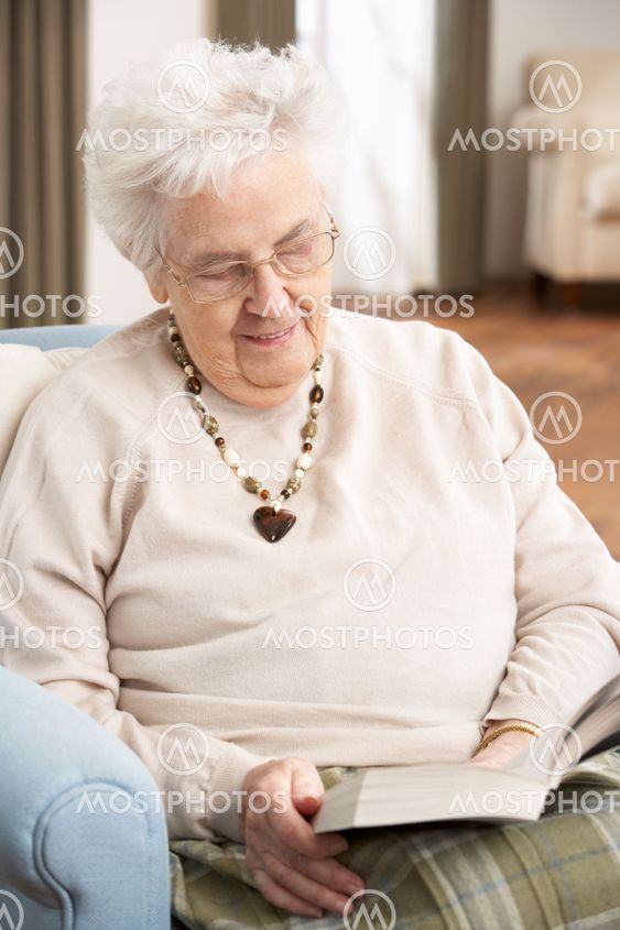 Senior Woman Relaxing In Chair At Home Reading Book