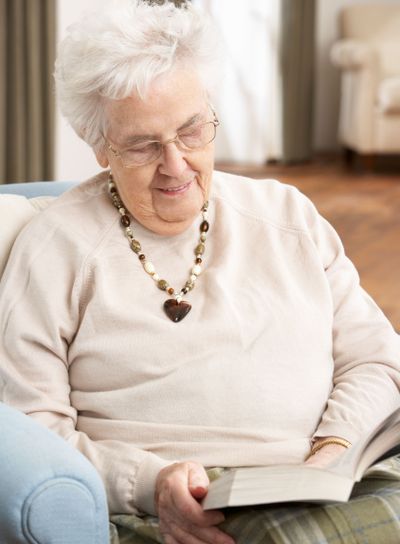 Senior Woman Relaxing In Chair At Home Reading Book