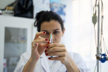 A focused nurse in a white lab coat carefully prepares a...
