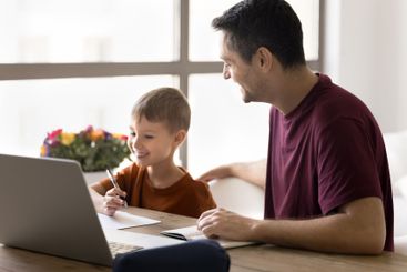 Smiling dad helps with online task to little son