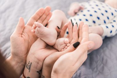 partial view of parents holding little babys feet in...