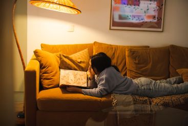 Side view of girl reading book under illuminated lamp...