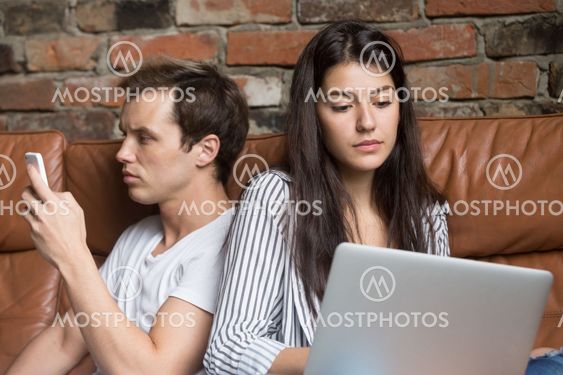Young couple sitting on couch addicted obsessed with modern gadg