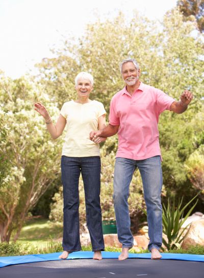Senior Couple Jumping On Trampoline In Garden