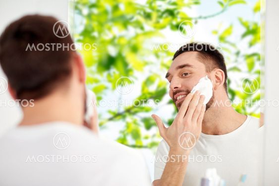 happy man applying shaving foam at bathroom mirror