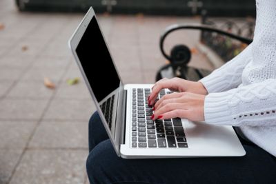 Laptop used by young woman hands sitting on bench outdoors