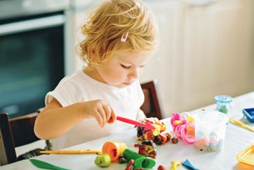 Adorable cute little toddler girl with colorful clay at...