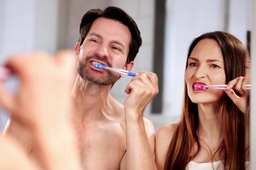 Man and woman smiling while brushing teeth in home bathroom