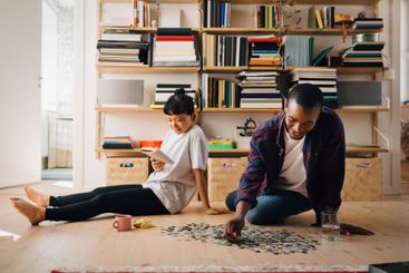 Man playing jigsaw puzzle while girlfriend reading book...
